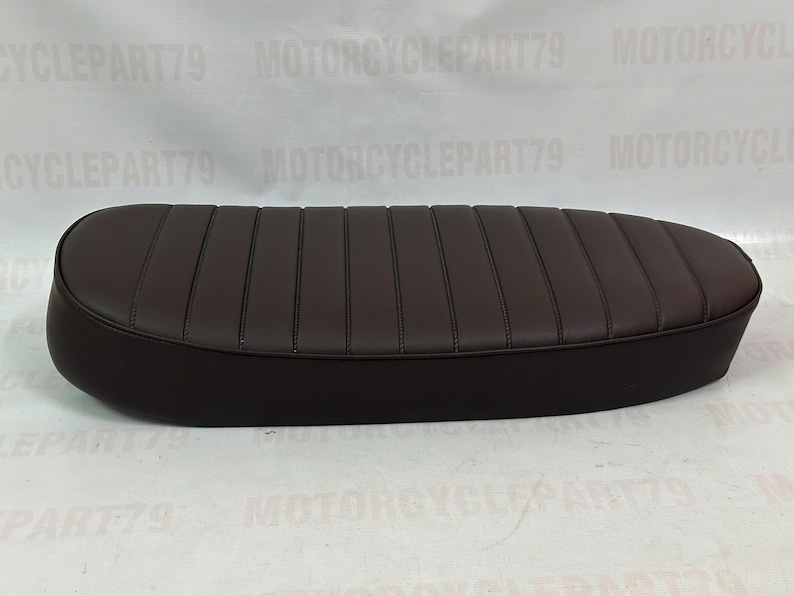 Peut inclure: Une selle de moto marron fonc&eacute; avec un design cousu et nervur&eacute;. La selle a une forme arrondie et est faite d'un mat&eacute;riau lisse. La selle est con&ccedil;ue pour une moto.
