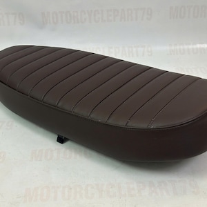 Peut inclure: Une selle de moto marron avec un design rembourr&eacute; et nervur&eacute;. Le si&egrave;ge est de forme ovale et semble &ecirc;tre fait de cuir ou d'un mat&eacute;riau similaire. La selle est de couleur marron fonc&eacute; et est con&ccedil;ue pour une moto.