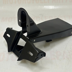 May include: A black motorcycle part, likely a bracket or support, with a curved top and rectangular base. It features multiple holes for mounting and a glossy finish. The part is designed for structural support.