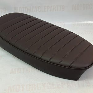 Peut inclure: Une selle de moto marron avec une surface rembourr&eacute;e et c&ocirc;tel&eacute;e. Le si&egrave;ge est de forme ovale et semble &ecirc;tre en cuir ou dans un mat&eacute;riau similaire. La selle est une pi&egrave;ce de rechange pour une moto.