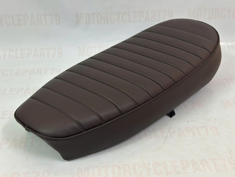 Peut inclure: Une selle de moto marron fonc&eacute; avec un design c&ocirc;tel&eacute;. La selle est de forme ovale et semble &ecirc;tre faite de cuir ou d'un mat&eacute;riau similaire. La selle est con&ccedil;ue pour un seul pilote.