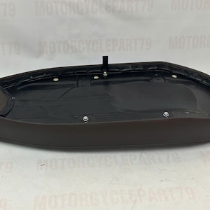 Peut inclure: Une selle de moto marron avec un int&eacute;rieur noir. La selle a une forme arrondie et est fix&eacute;e avec plusieurs fixations m&eacute;talliques. Un petit support noir est fix&eacute; sur le dessus de la selle.