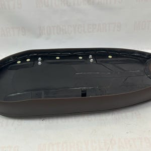 Peut inclure: Une selle de moto marron avec un int&eacute;rieur noir. La selle a une forme arrondie et est con&ccedil;ue pour s'adapter &agrave; une moto. La selle comporte plusieurs points de fixation et est fabriqu&eacute;e dans un mat&eacute;riau durable.