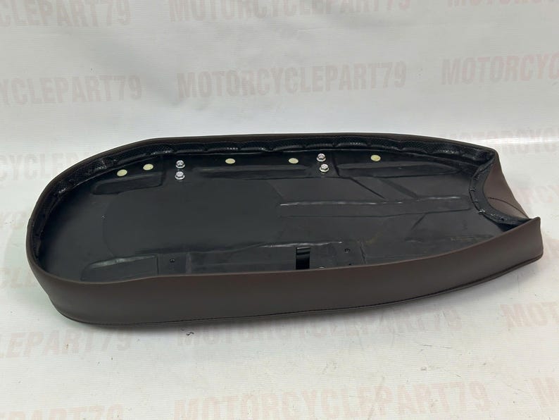 Peut inclure: Une selle de moto marron avec un int&eacute;rieur noir. La selle a une forme arrondie et est con&ccedil;ue pour s'adapter &agrave; une moto. La selle comporte plusieurs points de fixation et est fabriqu&eacute;e dans un mat&eacute;riau durable.