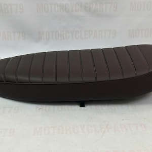 Peut inclure: Une selle de moto marron avec un design rembourr&eacute; et nervur&eacute;. Le si&egrave;ge est de forme ovale et semble &ecirc;tre en cuir ou dans un mat&eacute;riau similaire. Le si&egrave;ge est con&ccedil;u pour une moto et est une pi&egrave;ce de rechange.