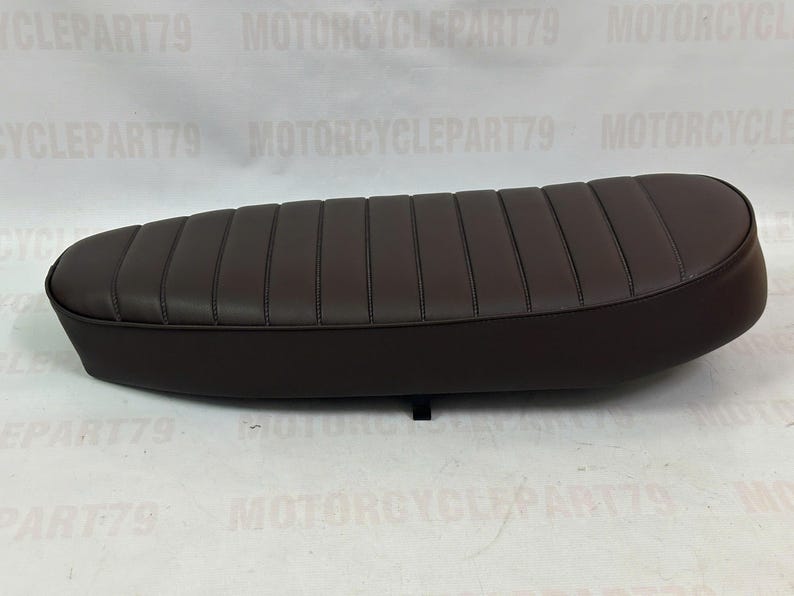 Peut inclure: Une selle de moto marron avec un design rembourr&eacute; et nervur&eacute;. Le si&egrave;ge est de forme ovale et semble &ecirc;tre en cuir ou dans un mat&eacute;riau similaire. Le si&egrave;ge est con&ccedil;u pour une moto et est une pi&egrave;ce de rechange.