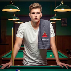 May include: A grey snooker towel featuring the text "STEPHEN'S SNOOKER TOWEL" and a graphic of a triangle of red snooker balls. The towel is draped over a person's shoulder in a snooker hall.
