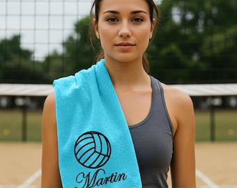 May include: A turquoise blue sports towel featuring a black volleyball design and the name "Martin" embroidered in black script. The towel is draped over a person's shoulder, with a volleyball net in the background.