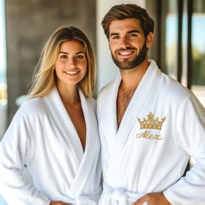 May include: Two white bathrobes with a gold crown and the name "Alex" embroidered on the front.