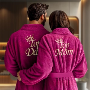 Könnte beinhalten: Zwei rosa Bademäntel mit goldener Stickerei. Der Bademantel links sagt "Top Dad" und der rechts "Top Mom".
