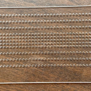 May include: A clear, rectangular ruler with evenly spaced holes, labeled "House of Smocking" and "Size K + Full Space Ruler." The ruler is made of transparent material and is designed for smocking projects.