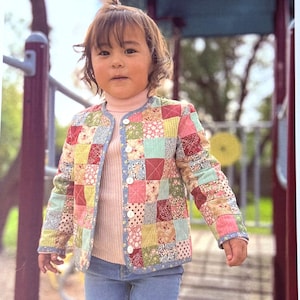 May include: A young child wearing a colorful patchwork jacket with the text "TIC TAC TOE CHILDREN'S PATCHWORK JACKET". The jacket has a button-up front and is made of various fabric squares in shades of pink, blue, yellow, and red.