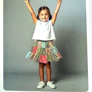 May include: A patchwork tiered skirt featuring various fabric squares in muted shades of pink, green, blue, and brown. The skirt has a gathered elastic waistband and a flared silhouette. The text TWIRL GIRL GIRLS PATCHWORK TIERED SKIRT and MELLY AND ME is visible.