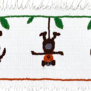 May include: Three brown monkeys hanging from a green vine with leaves. The monkeys have orange faces and gray bodies. The monkeys are embroidered on a white fabric.