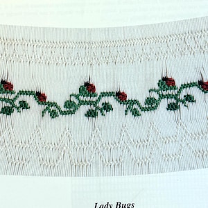 May include: A white fabric panel featuring smocking with a green vine and red ladybug embroidery pattern. The panel includes numbered rows from one to eight along the left side and the text Lady Bugs printed at the bottom center.