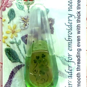 May include: A green Clover threader for embroidery needles. The tool has a clear plastic handle and a green body with a clover design. The packaging includes text that reads "Smooth threading even with thick threads."