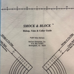 May include: A white paper sewing pattern guide with the text "SMOCK & BLOCK" and "Bishop, Yoke & Collar Guide". It includes curved lines, measurements, and text for smocking and pleating. The guide has a ruler along the top edge.