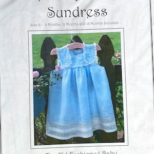 May include: A light blue baby sundress with white lace trim, displayed on a pink hanger. The image is from a pattern titled "French Acadian Sundress" by Jeannie Downs Baumeister. Sizes 6-9, 12, and 18 months are included.