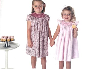 May include: A sewing pattern envelope titled BISHOP for sizes NB-24mo from Children's Corner Patterns. The cover features two dresses: one with a red floral print and smocked yoke, and one in solid light pink with a smocked yoke and flutter sleeves.
