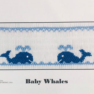 May include: A white embroidery pattern with two blue whales swimming in blue waves. The pattern is titled "Baby Whales" and includes the copyright information "Copyright USA, G. CROSSED CRICKET, 2014, Plate #337".