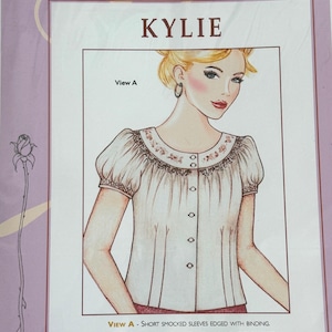 May include: A sewing pattern titled "KYLIE" for a smocked round yoke adult shirt. The illustration shows a woman wearing a white blouse with short, smocked sleeves. The pattern includes sizes 10, 12, 14, 16, and 18.
