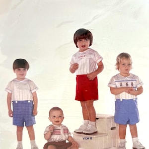 May include: A sewing pattern for boys' clothing, featuring four different views of a boy wearing a white shirt and shorts. The pattern is titled "Basics for Boys III".