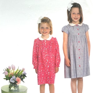 May include: Two young girls wearing dresses with white collars and button-up fronts. One dress is pink with a floral pattern, the other is blue with a dotted pattern. The image is from a pattern titled "RUTHIE" by "children's corner PATTERNS".