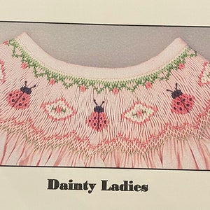 May include: A pink baby smocked dress with a white and green embroidered collar featuring ladybugs. The text "Dainty Ladies" is printed below the collar. The text "Copyright USA © CROSS EYED CRICKET, 2024 Plate #584" is printed in the bottom right corner.