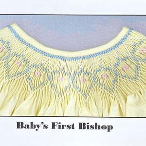 May include: A yellow baby dress with a detailed embroidered neckline. The neckline features a geometric pattern in white, light blue, and pink. The text "Baby's First Bishop" is printed at the bottom.