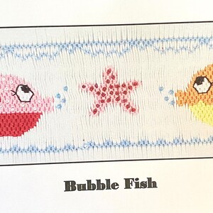 May include: A cross-stitch pattern for a "Bubble Fish" design. The pattern features two fish, a starfish, and bubbles. The fish are pink and orange with yellow accents. The starfish is pink with white accents. The pattern is on a white background with blue accents.