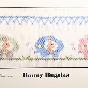 May include: A cross-stitch pattern featuring three bunny-shaped buggies. The buggies are green, blue, and pink, and each has a bunny inside. The pattern is titled "Bunny Buggies" and includes the copyright information "COPYRIGHT USA C CROSS-EYED CROCKET, 2010 Plate #229".