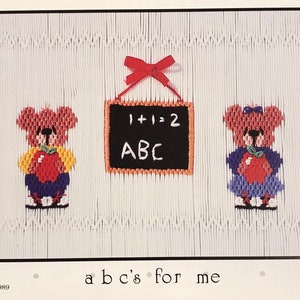 May include: A cross-stitch pattern featuring two teddy bears holding red apples, a chalkboard with the text "1+1=2 ABC" and the text "abc's for me".