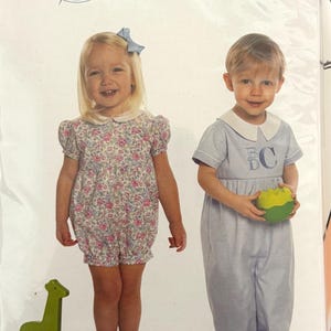 May include: A children's clothing pattern package featuring two young children. One child wears a floral romper, the other a blue jumpsuit. The package has the name "CHARLIE" and the sizes are 3 months to 3 years. A green wooden giraffe toy is in the image.