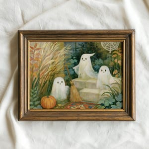 May include: A framed painting featuring three white ghosts in a garden setting with tall grasses, a broom, a pumpkin, and a spiderweb. The artwork is enclosed in a dark brown wooden frame with gold inner detailing, displaying a scene with green foliage.