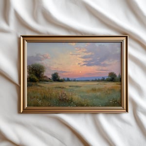 May include: A framed landscape painting depicts a sunset over a field. The artwork features a golden frame and a serene scene with a vibrant sky, trees, and a grassy meadow. The color palette includes warm oranges, blues, and greens.