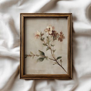 Puede incluir: Impresión floral enmarcada que presenta una rama con delicadas flores rosas y crema y hojas verdes. La obra de arte está enmarcada en un marco de madera marrón, creando una estética vintage.