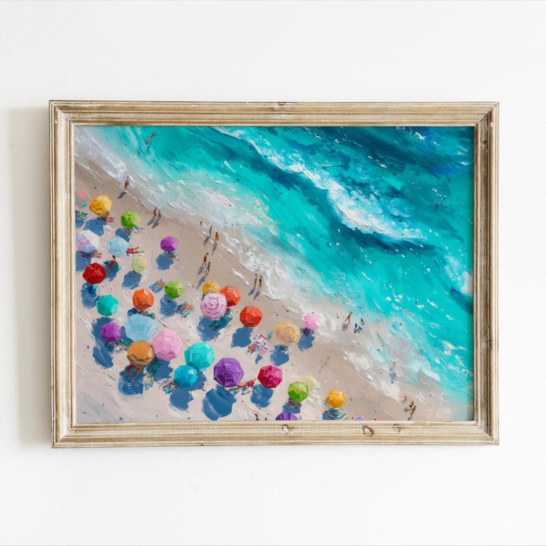 May include: A framed painting depicting a beach scene from above, with colourful parasols and figures. The artwork shows a turquoise sea with white waves meeting a sandy beach. The painting is set within a gold-coloured wooden frame.