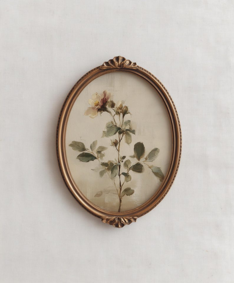 Puede incluir: Una impresi&oacute;n floral enmarcada de forma ovalada y de estilo antiguo. La obra presenta una delicada ilustraci&oacute;n bot&aacute;nica de una planta con flores con hojas verdes y una flor de color amarillo p&aacute;lido y rosa. El marco es dorado.