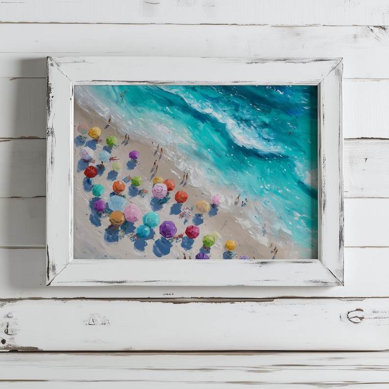 May include: A framed painting of a beach scene in a white, distressed frame. The artwork shows a sandy beach with colourful umbrellas and turquoise waves. People are scattered along the shore, enjoying the sunny day.