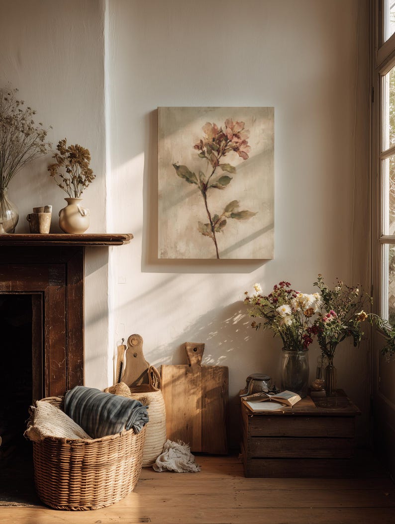 May include: A cozy interior scene featuring a floral painting, a woven basket with a blanket, and wooden cutting boards. Dried flowers in vases and a small wooden crate with a book add to the rustic aesthetic. The room is bathed in warm sunlight.