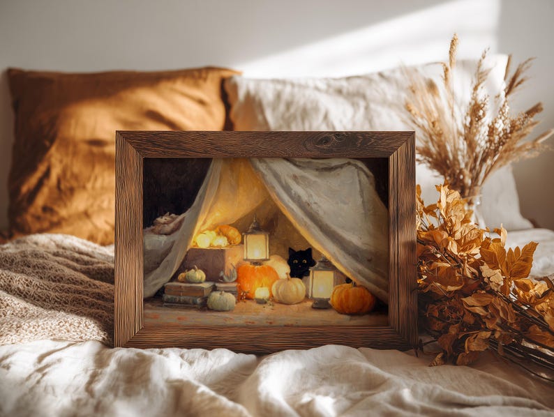 May include: A framed print showing a Halloween scene with a black cat, pumpkins, and lanterns under a draped canopy. The wooden frame surrounds the artwork, which has a warm colour palette of orange, yellow, and brown.