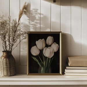 K&ouml;nnte beinhalten: Ein gerahmtes Gem&auml;lde von wei&szlig;en Tulpen in einer Vase vor einem dunklen Hintergrund. Der Rahmen ist golden und die Tulpen sind in einem Strau&szlig; angeordnet.