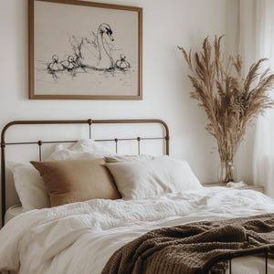 May include: A bedroom scene featuring a bed with white linens, brown pillows, and a brown knitted throw. Above the bed hangs a framed artwork depicting a swan and cygnets. A vase of dried plants sits on a nightstand.
