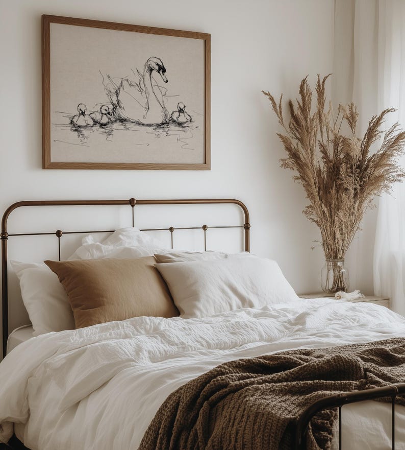 May include: A bedroom scene featuring a bed with white linens, brown pillows, and a brown knitted throw. Above the bed hangs a framed artwork depicting a swan and cygnets. A vase of dried plants sits on a nightstand.