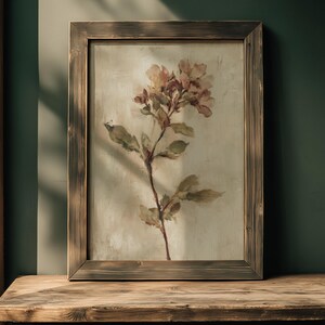 May include: A framed floral print featuring a delicate botanical illustration. The artwork showcases a stem with leaves and soft pink flowers against a neutral background. The wooden frame has a rustic, weathered appearance, adding to the vintage aesthetic.