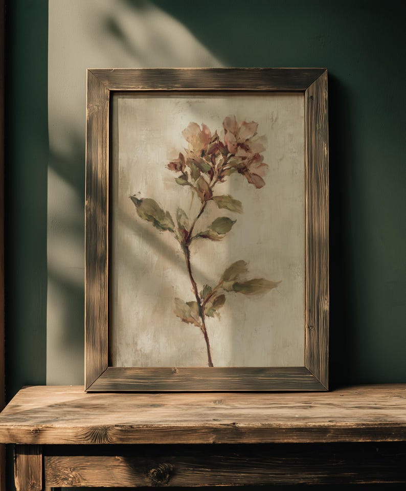 May include: A framed floral print featuring a delicate botanical illustration. The artwork showcases a stem with leaves and soft pink flowers against a neutral background. The wooden frame has a rustic, weathered appearance, adding to the vintage aesthetic.