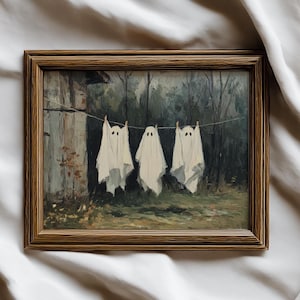 May include: A framed painting depicting three white ghost figures hanging on a washing line. The artwork has a vintage style, with a dark forest backdrop and a wooden frame. A whimsical Halloween theme.