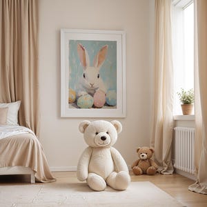 May include: A white teddy bear sitting on a beige rug in a room with a white bed, beige curtains, and a framed painting of a white rabbit with colorful Easter eggs.
