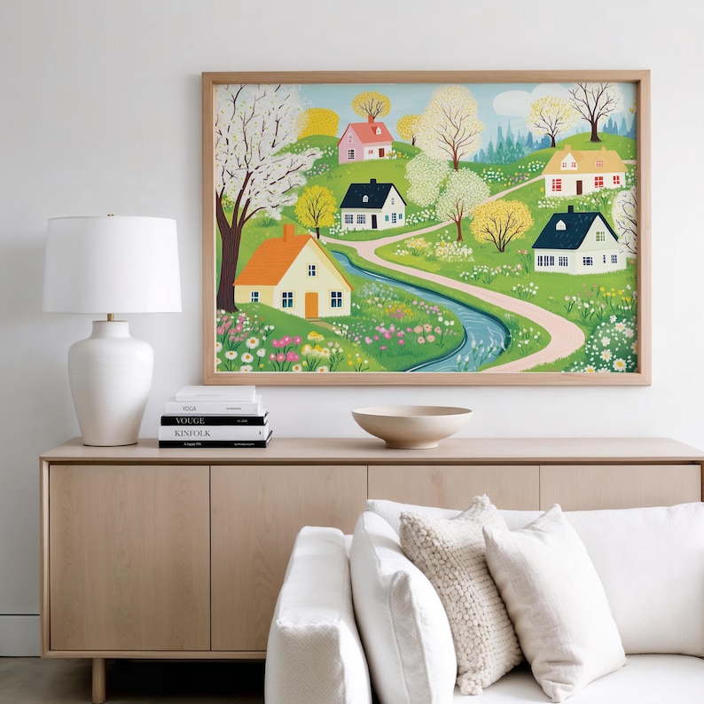 May include: A framed illustration of a whimsical village scene with colorful houses, winding paths, and a flowing stream. The houses are surrounded by lush green trees and blooming flowers in shades of pink, yellow, and white.