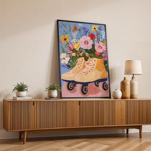 May include: A framed illustration of a pair of roller skates with a bouquet of colourful flowers in the skates. The background is a light blue colour. The roller skates are light yellow and have black wheels. The flowers are pink, yellow, orange, and purple. The illustration is hanging on a wall above a wooden cabinet.